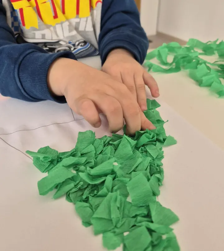 Copil care lipește hârtie creponată verde pe un contur