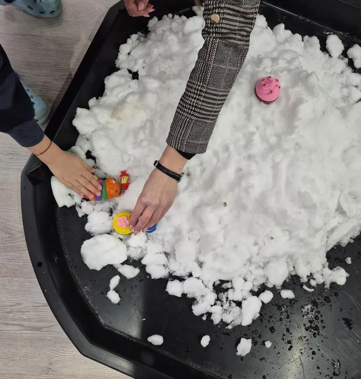 Mâini de copil care explorează zăpadă artificială cu jucării